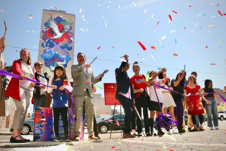 Confetti is visible in the air as people celebrate in front of a mural on a building.