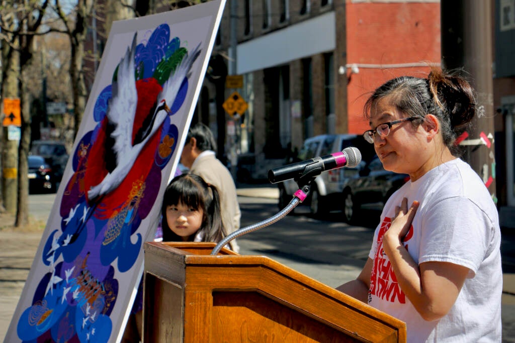 Yvonne Lung speaks at a podium, next to a small replica of the mural she helped create.