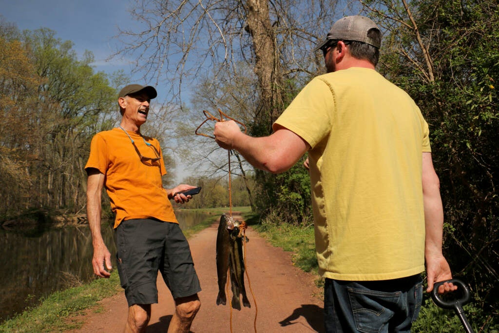 Neil King talking with a fisherman who is holding up fish he caught.