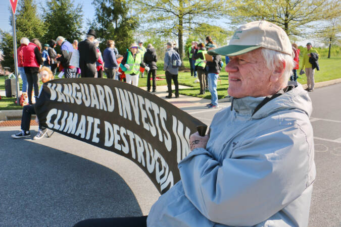 George Lakey, 85, of Philadelphia, holds a banner denouncing Vanguard's investment strategies, during a protest outside Vanguard offices near Malvern, Pa. (Emma Lee/WHYY)