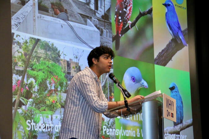 Aman Sharma speaks from a podium in front of a presentation featuring different photos of birds and gardens.