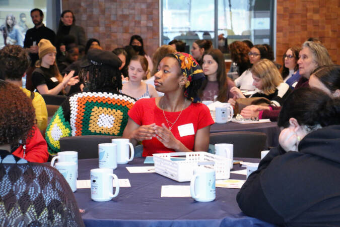 High school students seated at tables look on.