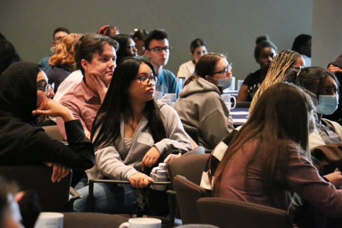 High school students seated in an audience look forward, listening.