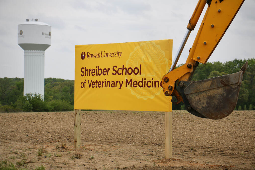 A sign reads "Shreiber School of Veterinary Medicine in a field. An excavator is visible in the foreground.