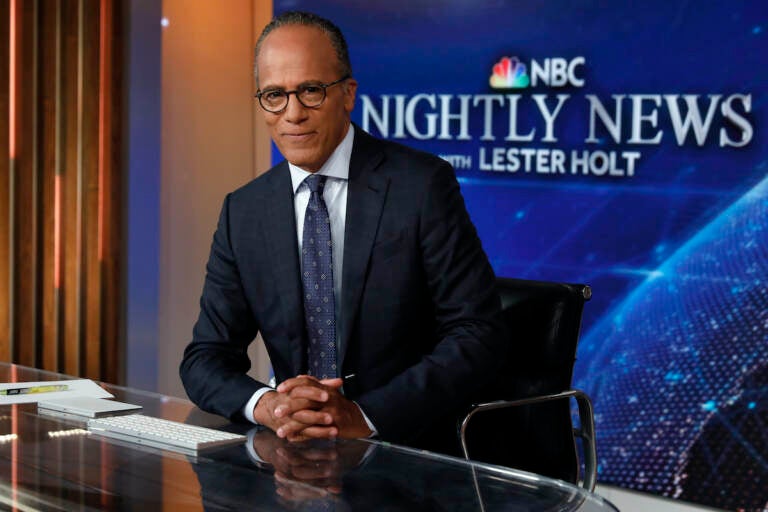 Lester Holt sits at the desk with a sign for NBC Nightly News in the background.