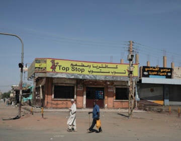 People walk past shuttered shops in Khartoum, Sudan