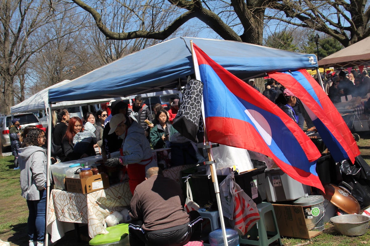 two flag of the nation of Laos fly in the wind, attached to a vendor's tent at the SouthEast Asian Market at FDR Park in Philadelphia