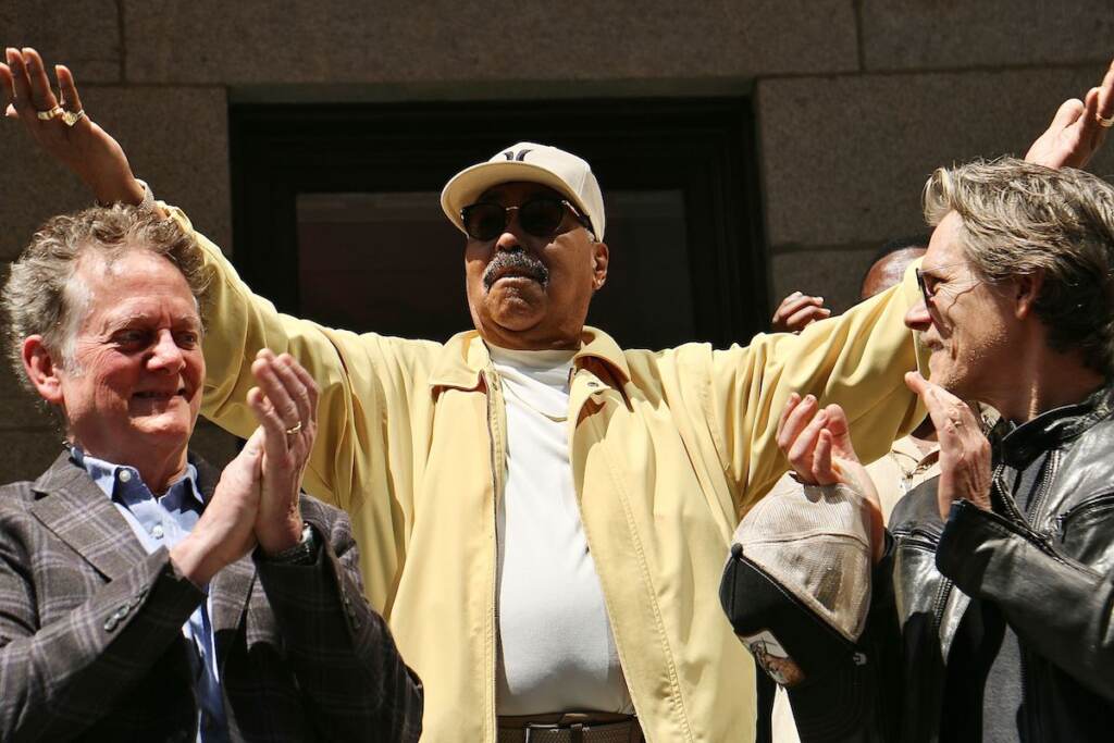 Norman Burnett raises his arms in celebration as he and his a cappella group, The Tymes, are honored with a star on Philadelphia Music Alliance Walk of Fame. Applauding are the Bacon brothers, Michael (left) and Kevin, who were also honored