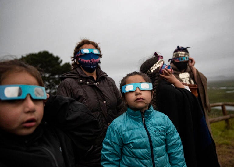 A Mapuche Indigenous family uses special glasses to try and observe a total solar eclipse in Carahue, La Araucania, Chile, Monday, Dec. 14, 2020. The total eclipse was barely visible from Carahue because of an overcast sky. (AP Photo/Esteban Felix)