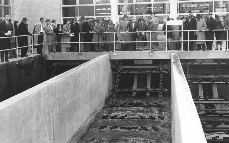 A black-and-white photo of people overlooking a sewage plant.