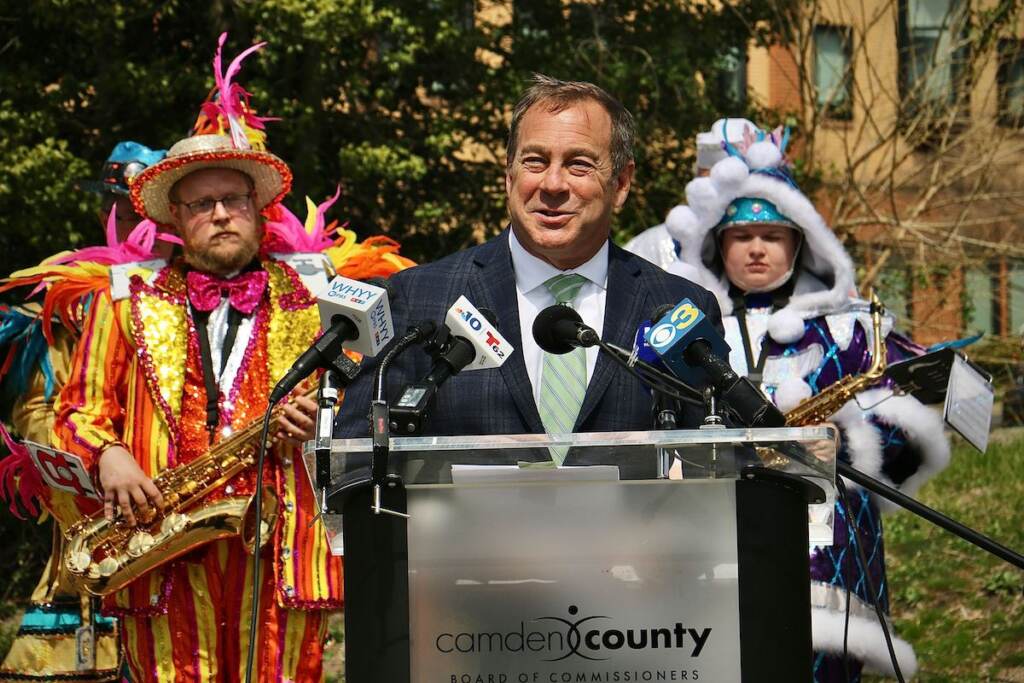 Louis Cappelli speaks at a podium. People wearing colorful costumes stand behind him.