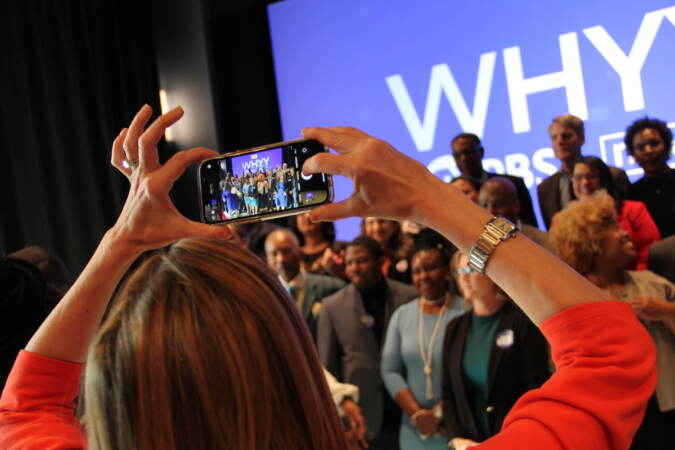 A person holds up a phone and takes a photo of a group of people.