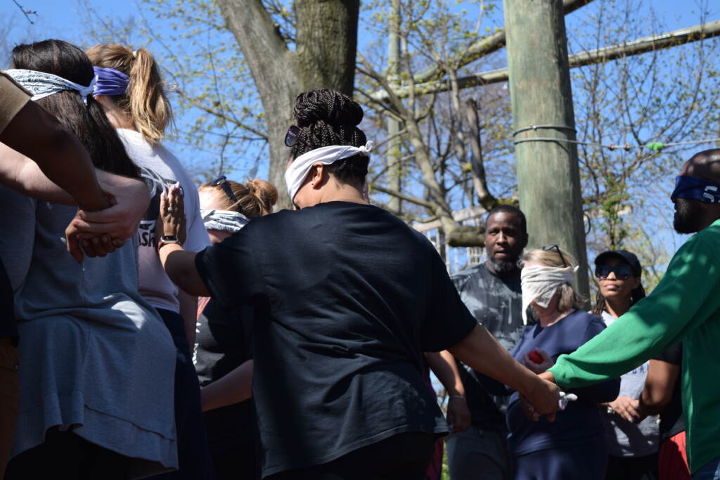 Several people are holding hands in a park while blindfolded.