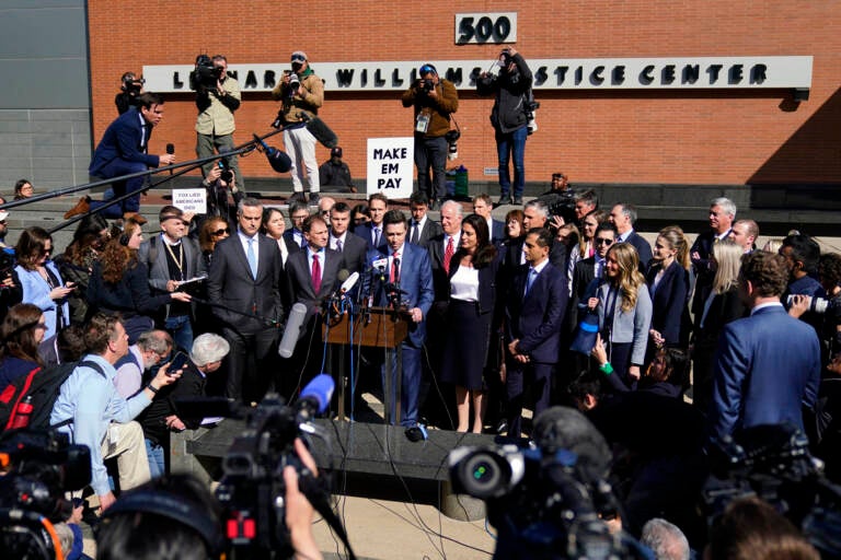 People stand in a group surrounded by cameras and news reporters.