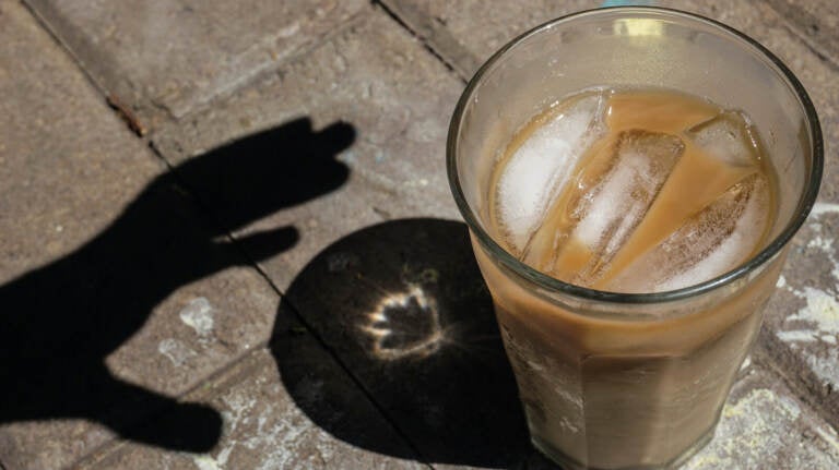 Shadow of a hand reaching for an iced coffee