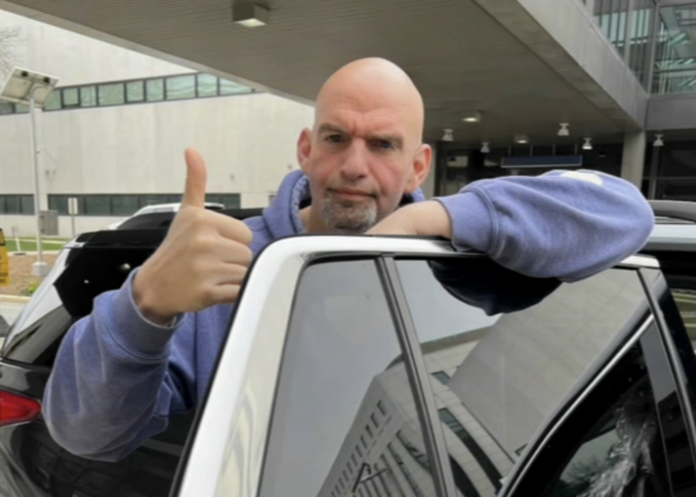 John Fetterman gives a thumbs up while getting into a car.