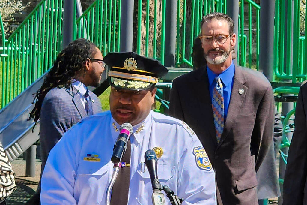 John Stanford speaking at a podium during a press conference.