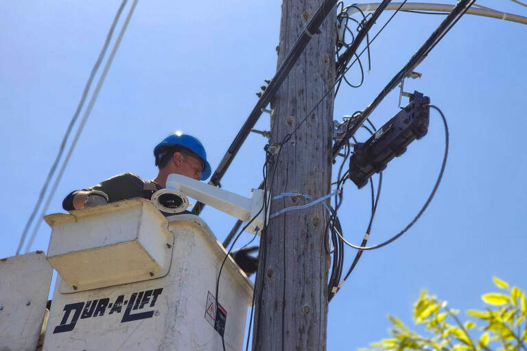 A worker is setting up a security camera to a telephone poll.