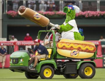 The Phillie Phanatic rides on a cart on field with the hot dog cannon in hand.