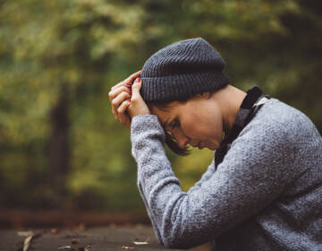 A person sits with their head in their hands in a forest.