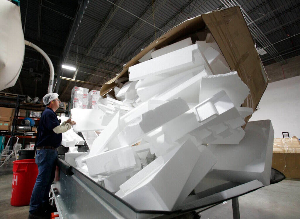 Piles of styrofoam containers are visible in a recycling machine.