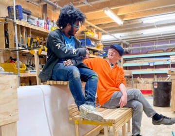 Two people sit on benches in a workshop.
