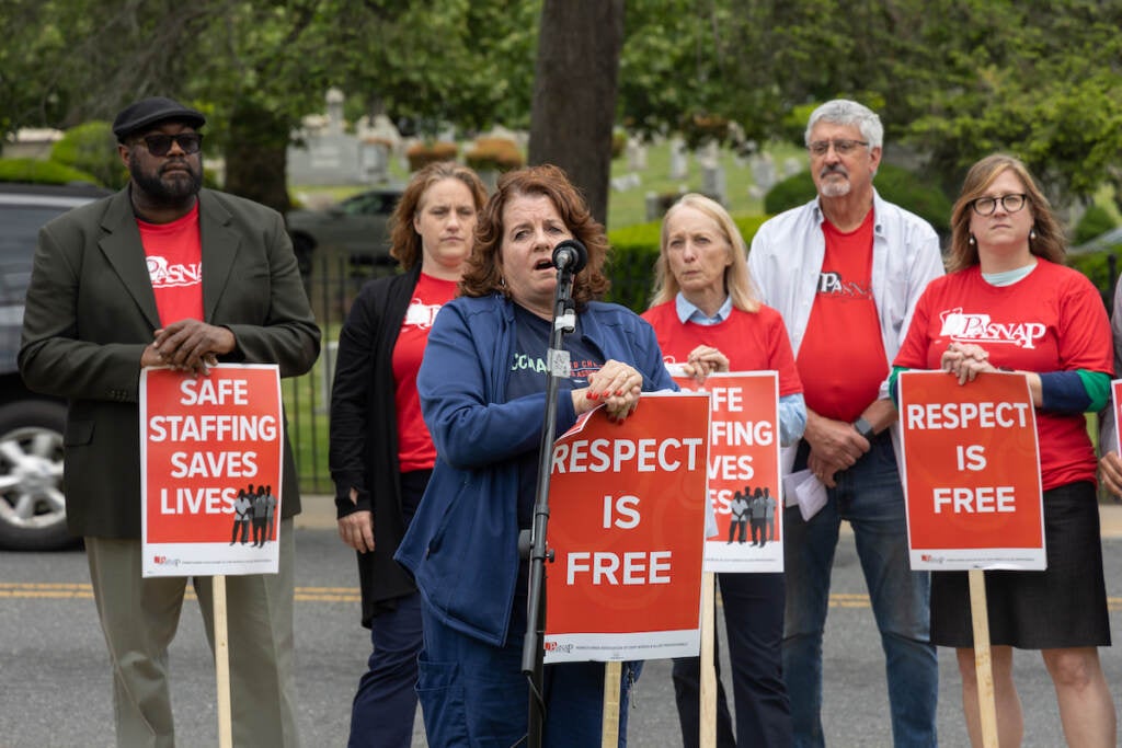 RN Peggy Malone speaks into a microphone as other protesters gather around her.