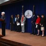 State Sen. Carloyn Comitta stands at a podium as other lawmakers and officials look on from behind her.