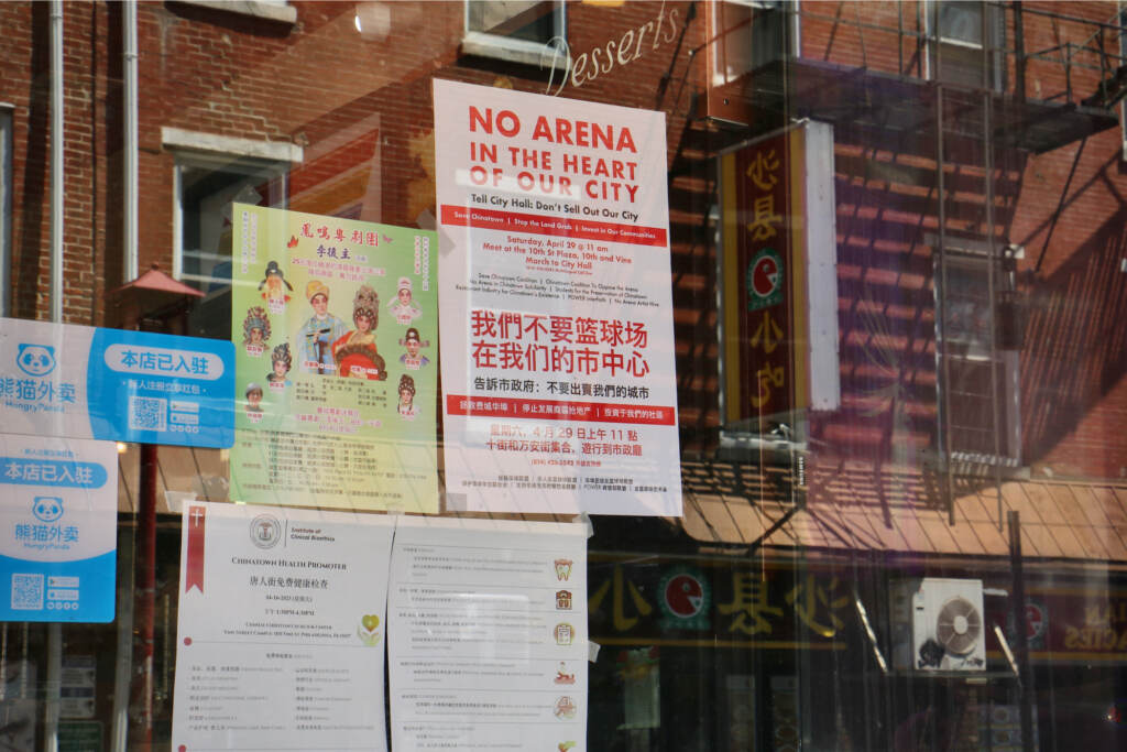 Signs against the 76ers arena being built in Chinatown are placed in a window.
