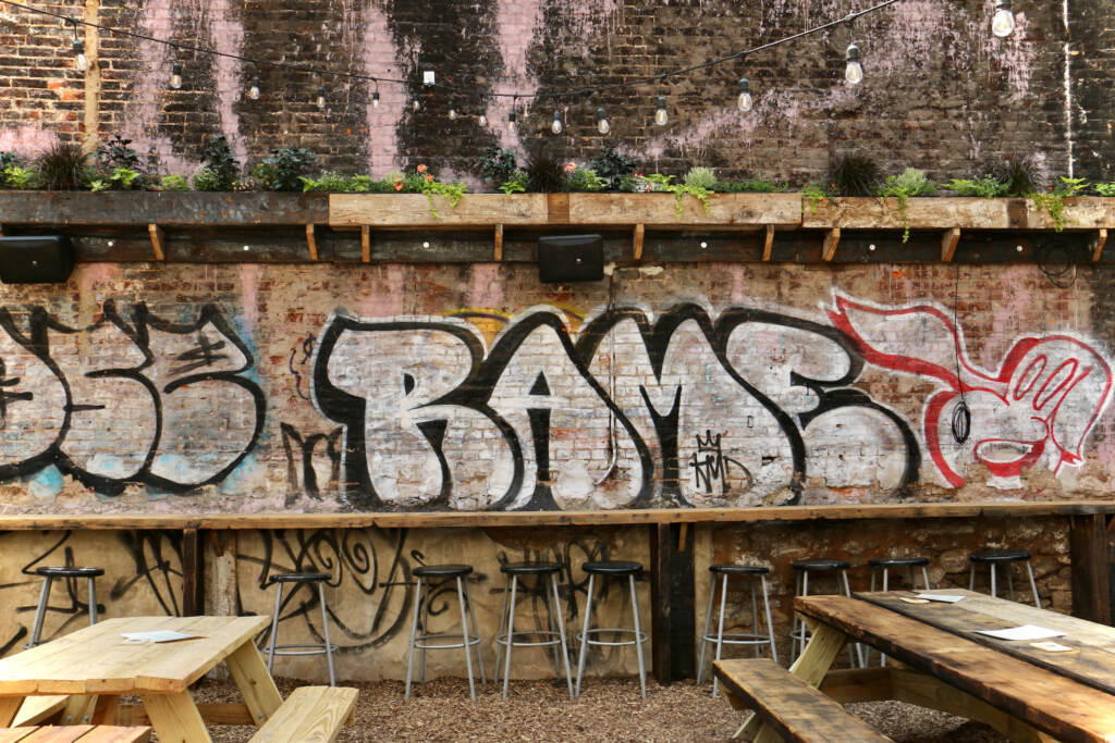 Graffiti is visible on a wall outdoors. Picnic tables are visible in the foreground.