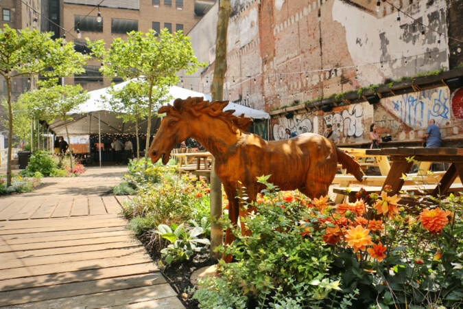 A sculpture of a horse is visible amid flowers in an outdoor area.