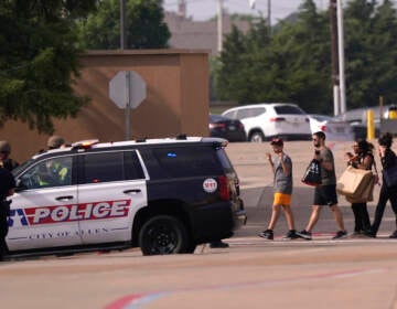 People raise their hands as they leave a shopping center following reports of a shooting, Saturday, May 6, 2023, in Allen, Texas.