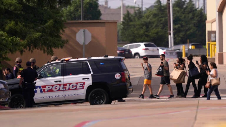 People raise their hands as they leave a shopping center following reports of a shooting, Saturday, May 6, 2023, in Allen, Texas.