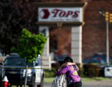 People hug outside the scene after a shooting at Tops supermarket, May 14, 2022, in Buffalo, N.Y. The city of Buffalo will pause Sunday, May 14, 2023 to mark the passing of one year since a gunman killed 10 people and injured three others in a racist attack that targeted Black people at a city supermarket