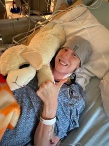 Ashley Yeager lies on a hospital bed with her hand in a thumbs up position. 