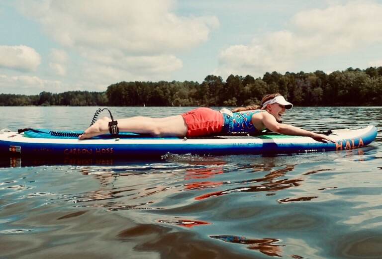 Ashley Yeager lies on a paddle board on a lake.