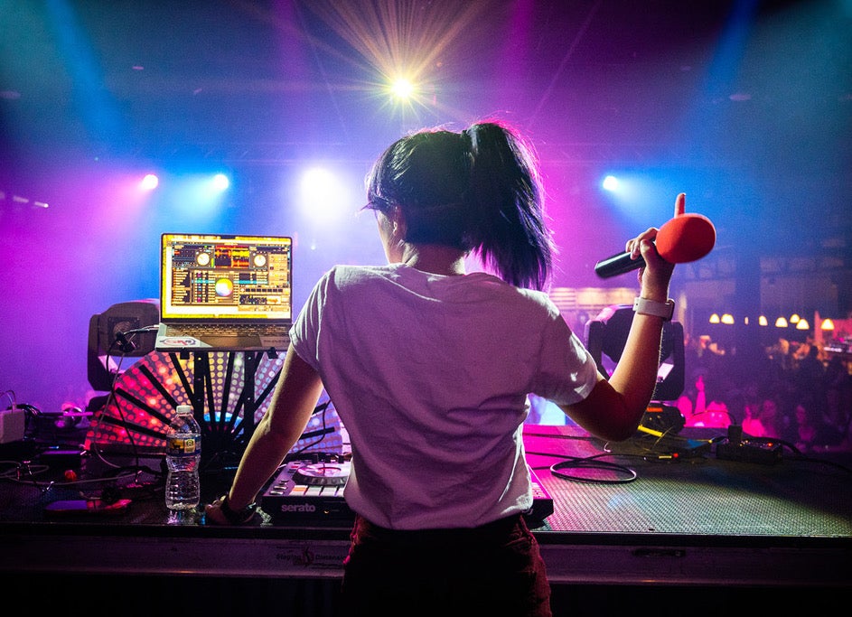 A DJ plays music as people dance below on the floor.