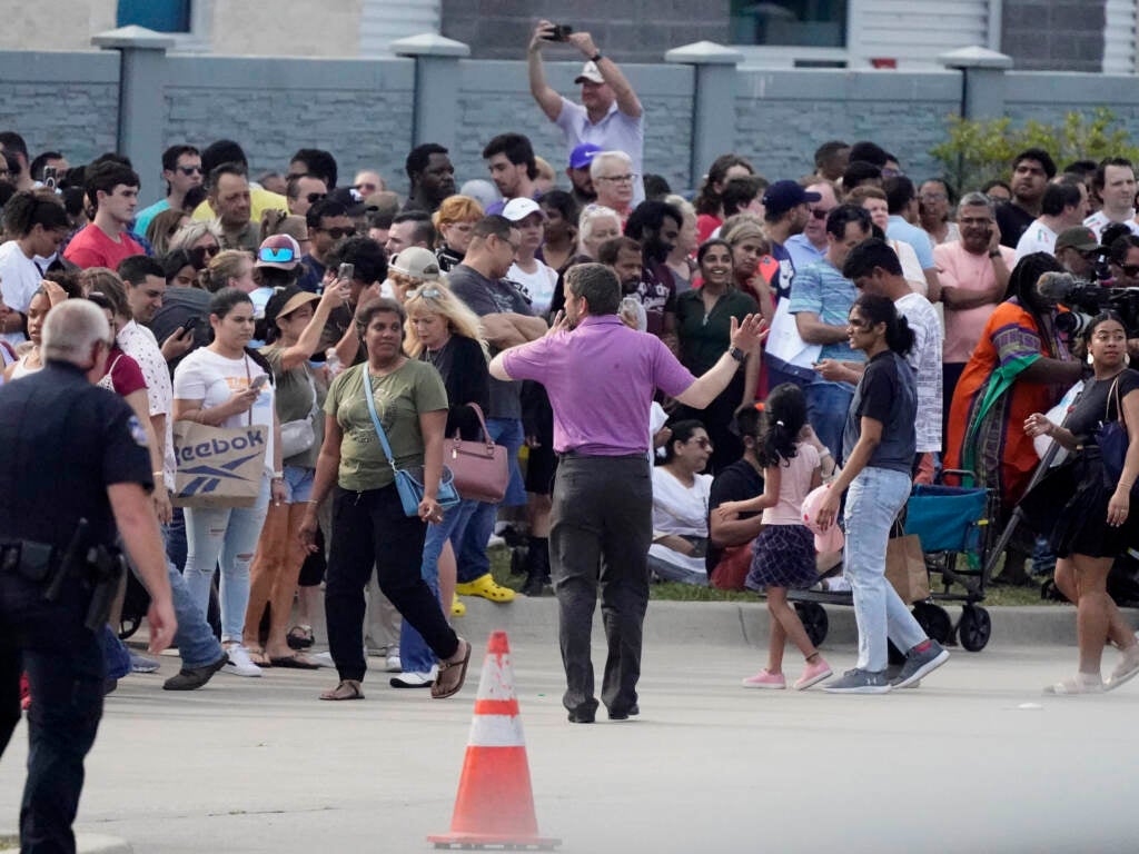 People gather across the street from a shopping center after the shooting on Saturday in Allen, Texas