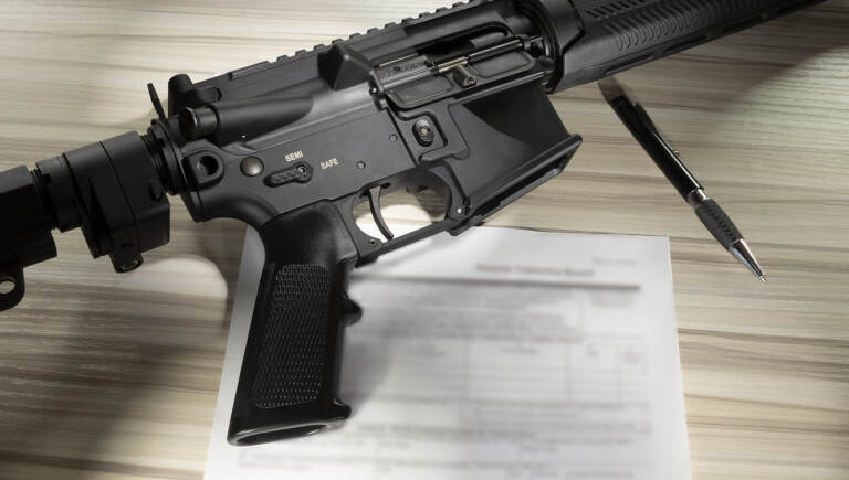 An assault rifle is shown along with paperwork