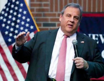 Chris Christie speaks into a microphone. A U.S. flag is visible behind him.