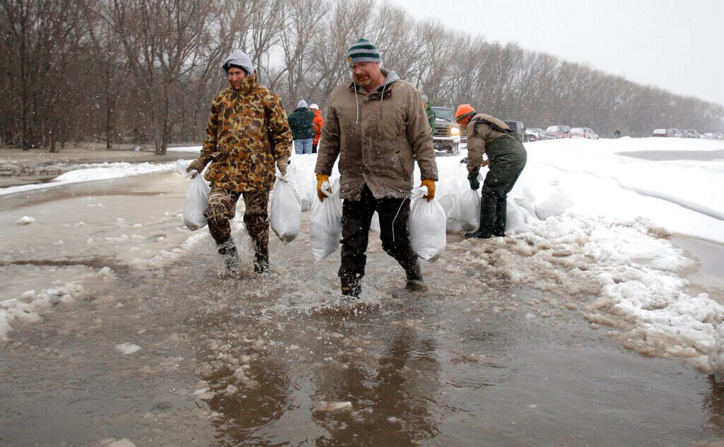 People carry sand bags in a flooded area.