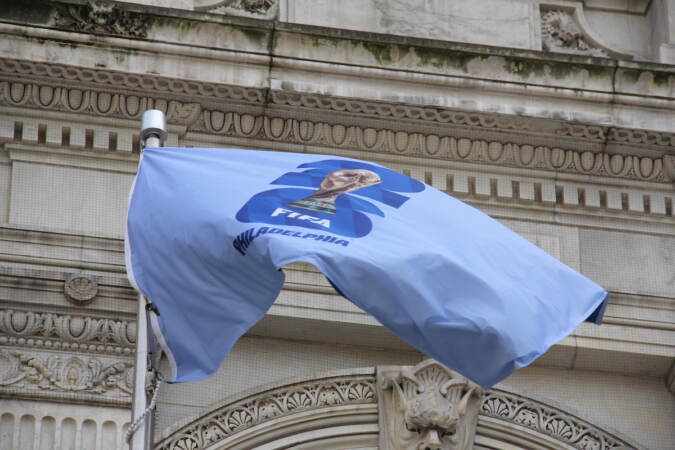 The FIFA World Cup flag flies in the wind. The flag is emblazoned with the World Cup trophy on a baby blue background.