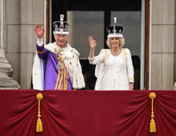 Britain's King Charles III wearing the Imperial state Crown, and Britain's Queen Camilla wearing a modified version of Queen Mary's Crown wave from the Buckingham Palace balcony after viewing the Royal Air Force fly-past in central London on Saturday. Oli Scarff/AFP via Getty Images