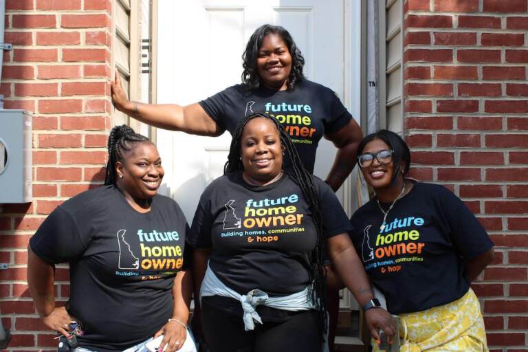 People pose, smiling for a photo outside of a house.