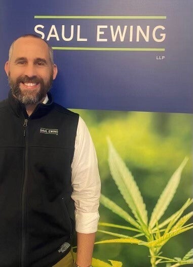 Peter Murphy poses in front of a sign which depicts an image of the marijuana plant.