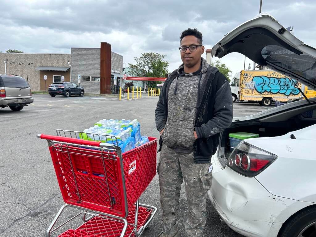 William Huarcaya stands with a cart full of bottled water near his car.