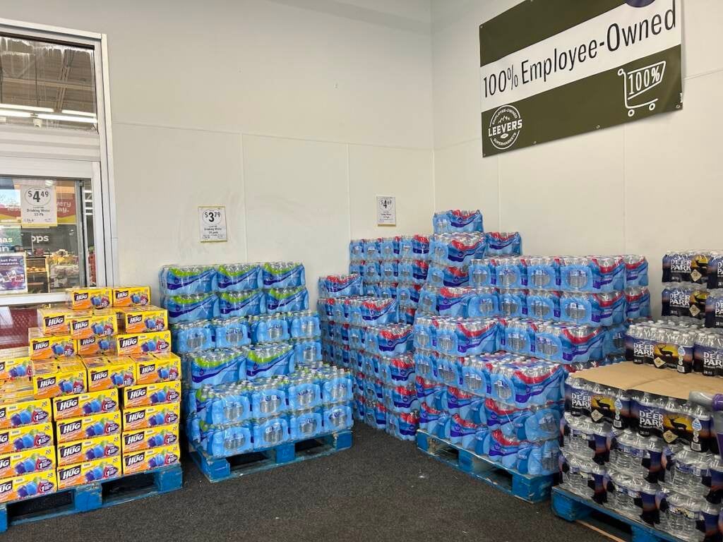 Cases of bottled water are stacked on top of one another in a corner.