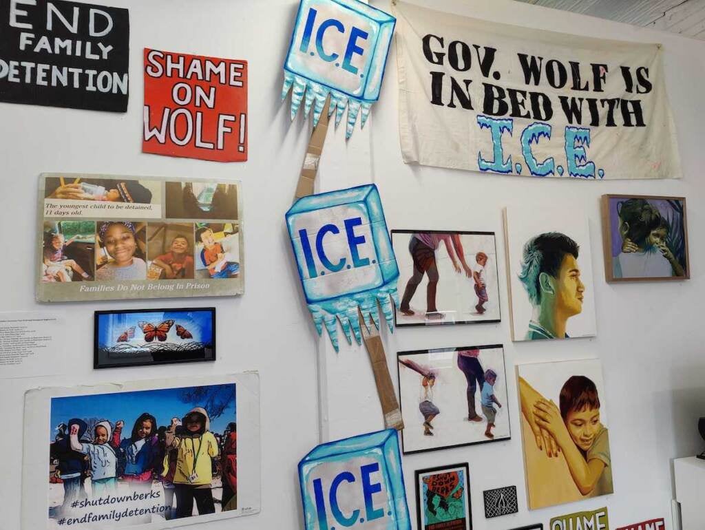 SIgns criticizing ICE and Gov. Wolf are displayed on a wall along with other artworks.