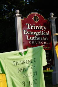A t-shirt with a name, age, and date of death in front of a church's sign