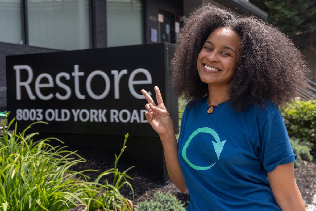 Lyndsay Alston gives the peace sign as she poses for a photo next to a sign that reads "Restore."